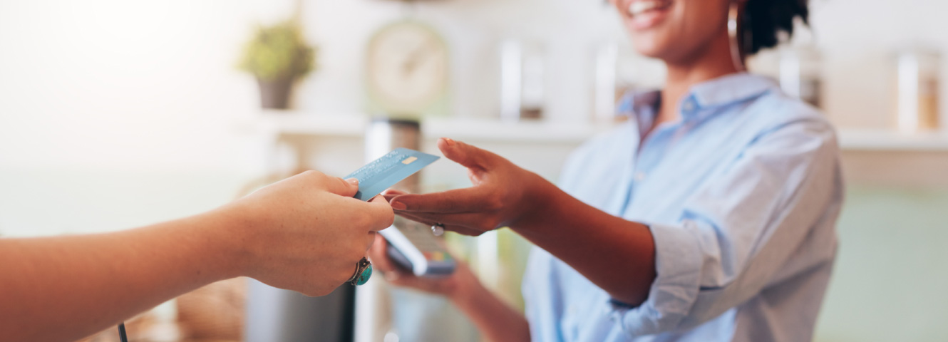 Close up of someone's hand holding out a credit card for a woman with a card reader.