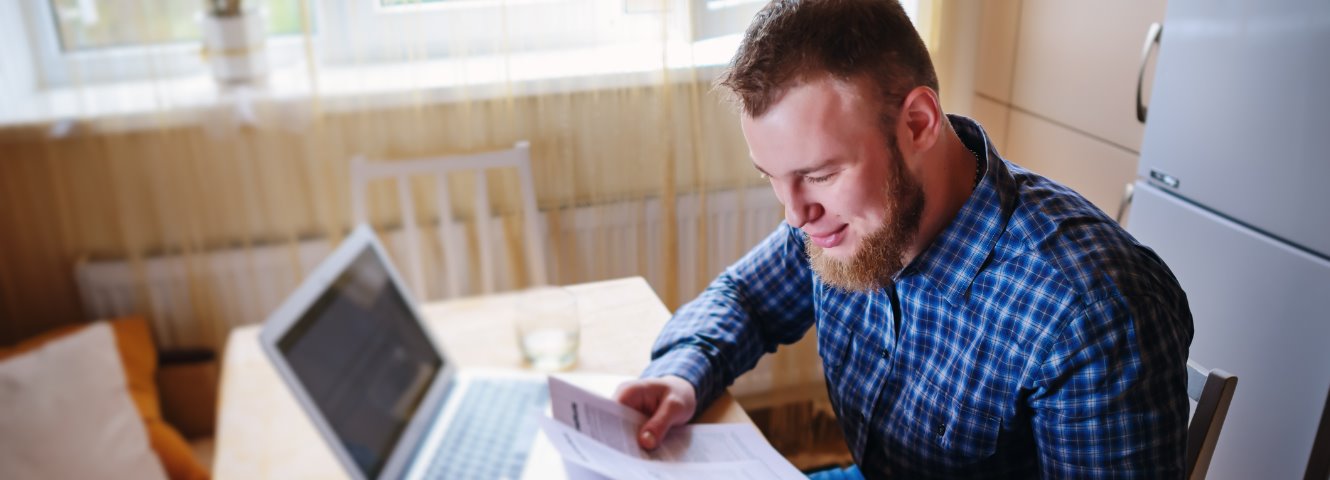 man sitting at computer looking at bills