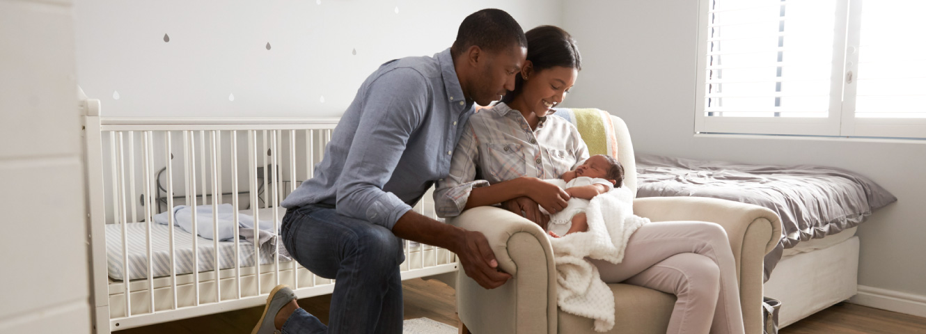 A new mother and father hold their baby in a white room.